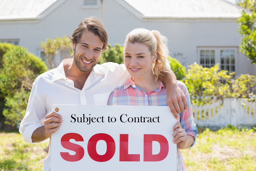 Two home owners with a Sold subject to contract sign